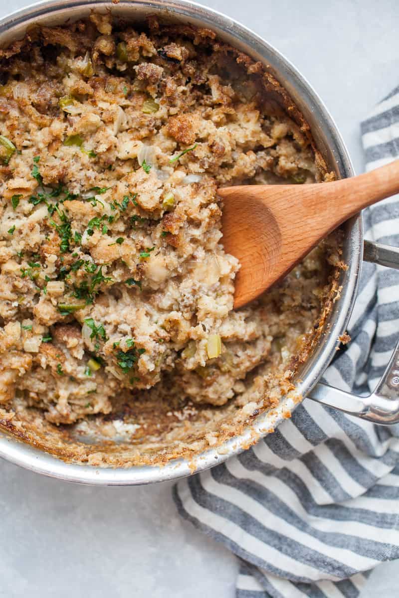 Close-up of sausage stuffing being scooped from a baking dish, showing the golden crispy top and soft herby interior with visible pieces of Italian sausage