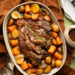 Slow cooker pot roast served on a large platter with tender carrots, potatoes, and onions, topped with glossy dark gravy, garnished with fresh thyme