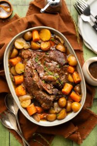 Slow cooker pot roast served on a large platter with tender carrots, potatoes, and onions, topped with glossy dark gravy, garnished with fresh thyme