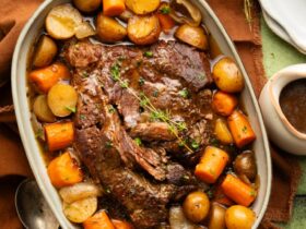 Slow cooker pot roast served on a large platter with tender carrots, potatoes, and onions, topped with glossy dark gravy, garnished with fresh thyme