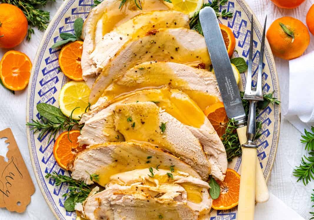 Slow cooker turkey breast sliced on a wooden cutting board with fresh herbs, golden skin, and rich pan gravy drizzled over the top
