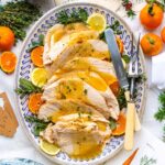 Slow cooker turkey breast sliced on a wooden cutting board with fresh herbs, golden skin, and rich pan gravy drizzled over the top
