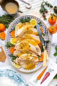 Slow cooker turkey breast sliced on a wooden cutting board with fresh herbs, golden skin, and rich pan gravy drizzled over the top