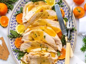 Slow cooker turkey breast sliced on a wooden cutting board with fresh herbs, golden skin, and rich pan gravy drizzled over the top