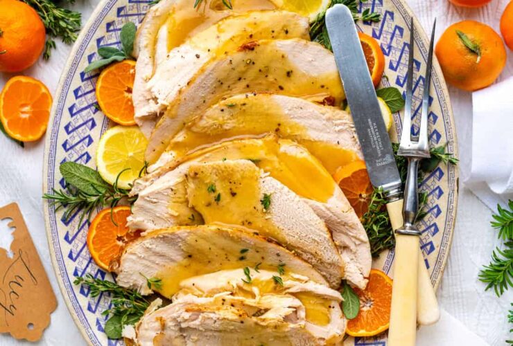 Slow cooker turkey breast sliced on a wooden cutting board with fresh herbs, golden skin, and rich pan gravy drizzled over the top