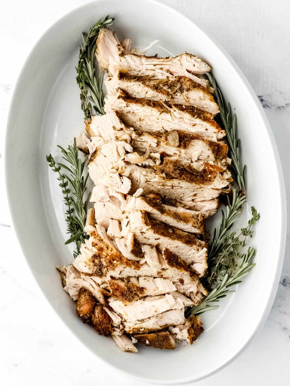 Overhead flat lay of slow cooker turkey breast ingredients — herb butter, fresh rosemary, thyme, garlic, onion, and raw turkey breast on a marble surface