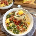 Slow cooker Zuppa Toscana served in a rustic bowl with creamy broth, Italian sausage, potato slices, and wilted kale, garnished with Parmesan and red pepper flakes