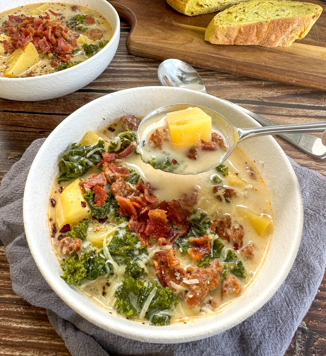 Slow cooker Zuppa Toscana served in a rustic bowl with creamy broth, Italian sausage, potato slices, and wilted kale, garnished with Parmesan and red pepper flakes