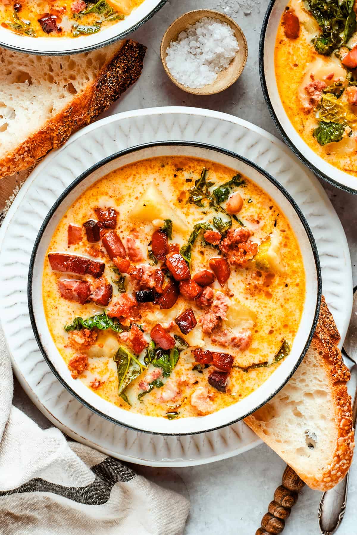 Slow cooker Zuppa Toscana ingredients laid out on a wooden surface — Italian sausage, russet potatoes, kale, garlic, chicken broth, and heavy cream