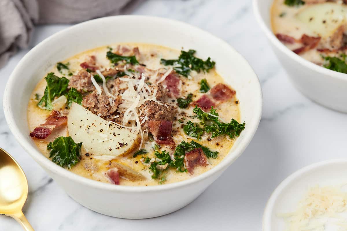 Close-up of a ladle lifting creamy Zuppa Toscana broth with a slice of potato and sausage, steam rising, Parmesan shavings on top