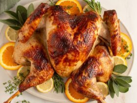 Beautifully plated whole spatchcock turkey on a large wooden serving board with fresh rosemary, thyme, sliced citrus, and pan drippings poured over the skin, golden brown and crispy