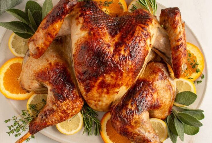 Beautifully plated whole spatchcock turkey on a large wooden serving board with fresh rosemary, thyme, sliced citrus, and pan drippings poured over the skin, golden brown and crispy