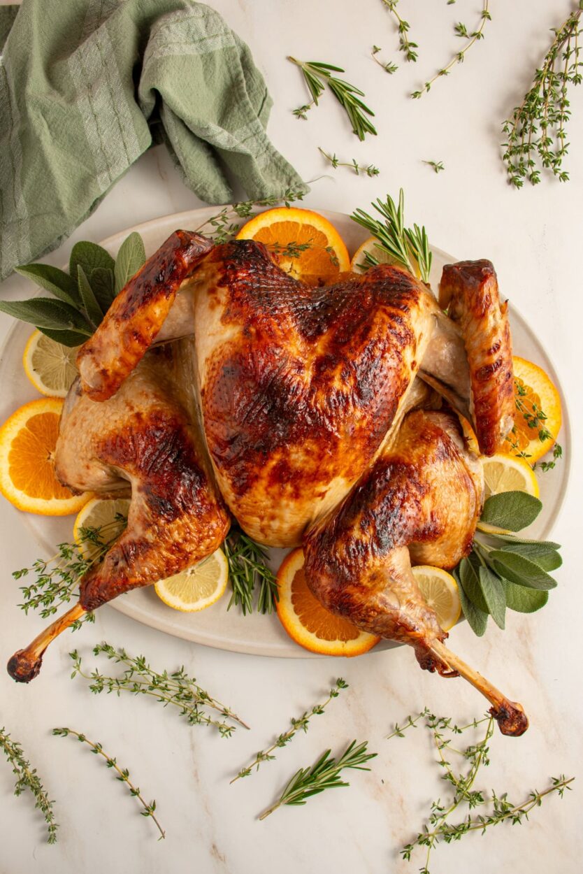 Beautifully plated whole spatchcock turkey on a large wooden serving board with fresh rosemary, thyme, sliced citrus, and pan drippings poured over the skin, golden brown and crispy