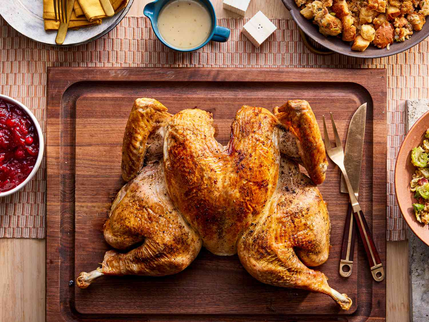 Step-by-step flat-lay of spatchcock turkey preparation: backbone removed with kitchen shears, herb butter ingredients spread on a cutting board, turkey pressed flat on a large roasting rack