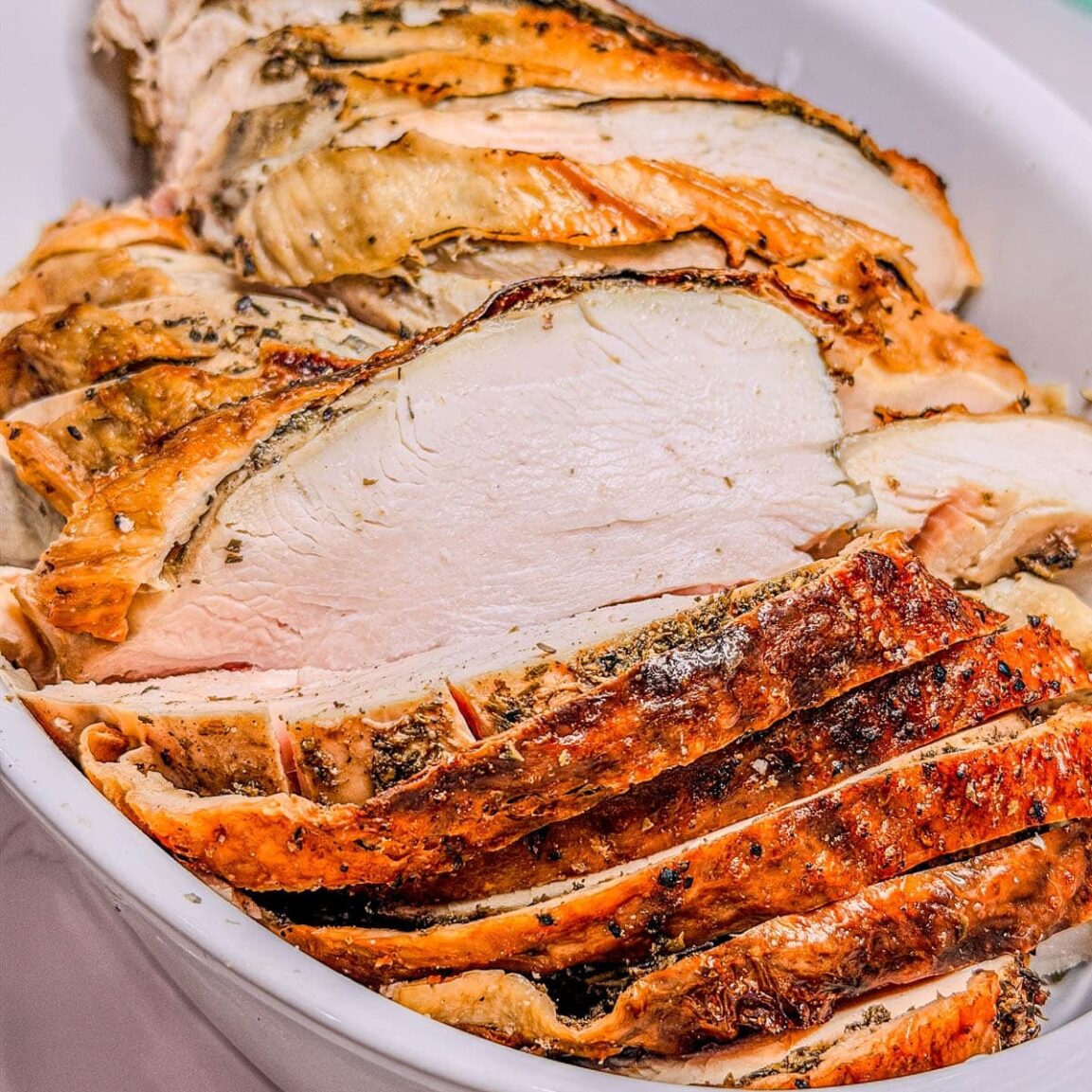 Close-up serving shot of spatchcock turkey sliced on a wooden board, showing juicy breast meat and crispy golden skin, with fresh herbs and roasted garlic cloves scattered around