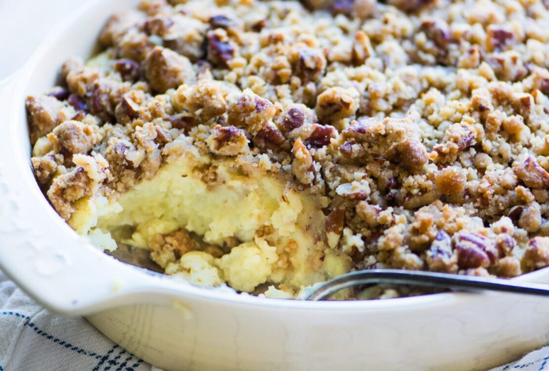 Sweet potato casserole with pecan streusel in a white baking dish, golden brown crust, fresh from the oven with a spoon lifting a scoop