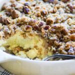 Sweet potato casserole with pecan streusel in a white baking dish, golden brown crust, fresh from the oven with a spoon lifting a scoop