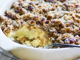 Sweet potato casserole with pecan streusel in a white baking dish, golden brown crust, fresh from the oven with a spoon lifting a scoop