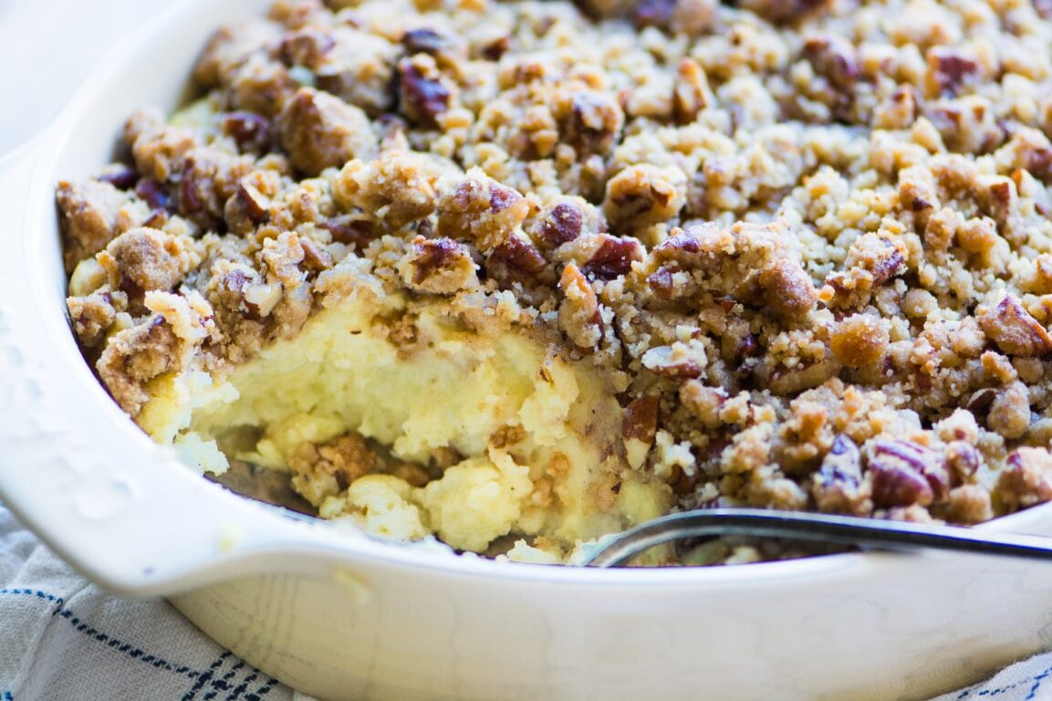 Sweet potato casserole with pecan streusel in a white baking dish, golden brown crust, fresh from the oven with a spoon lifting a scoop