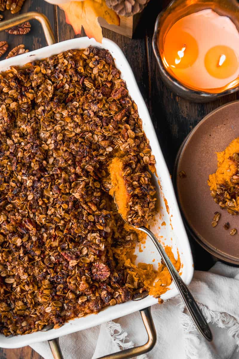 Overhead flat lay of sweet potato casserole ingredients — whole sweet potatoes, pecans, brown sugar, butter, eggs, vanilla, and cream on a marble surface