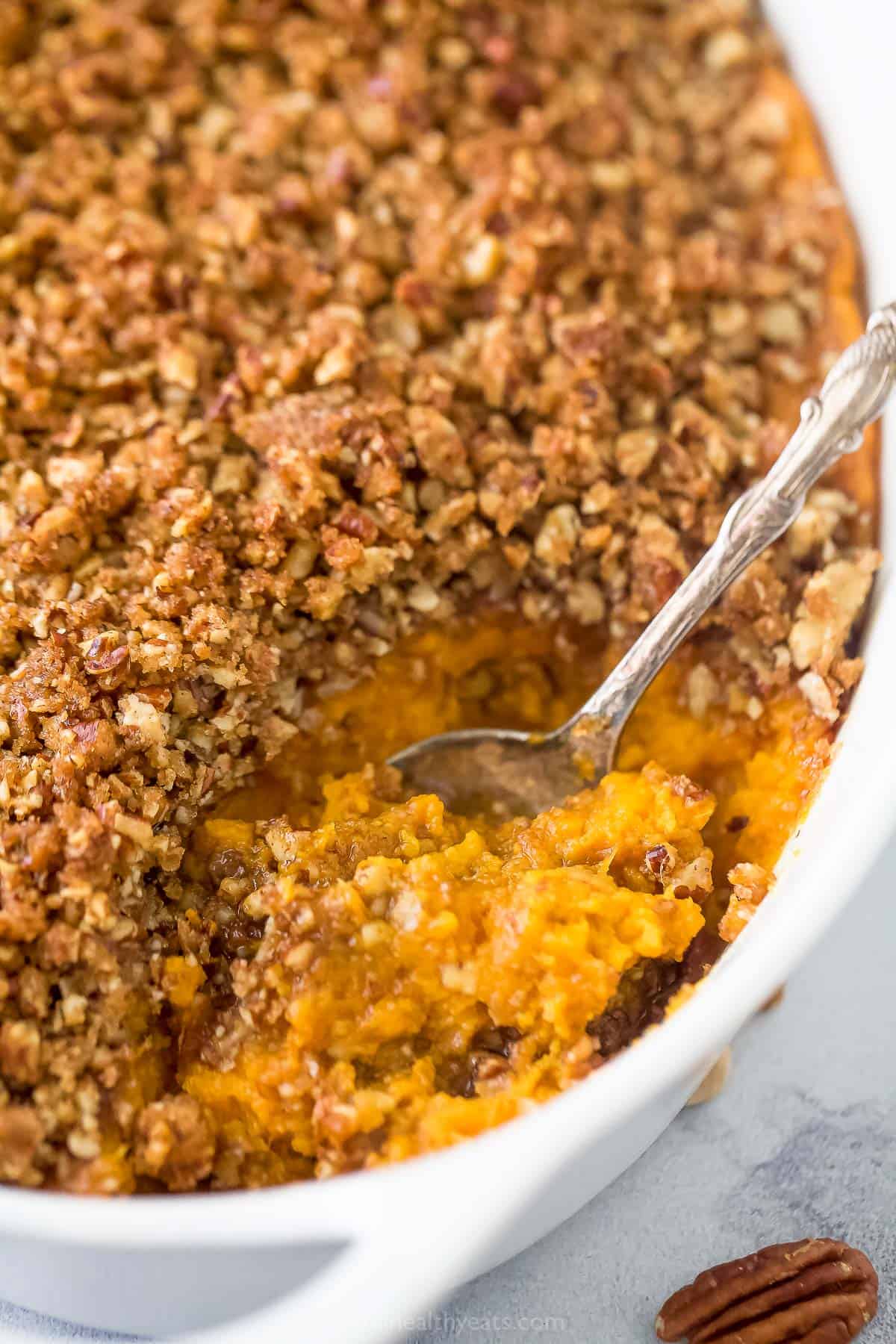 Close-up of a spoonful of sweet potato casserole being lifted from the dish, showing the creamy orange filling and golden pecan streusel crust in detail