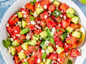 Watermelon Feta Salad served on a large white platter with crumbled feta, fresh mint, cucumber slices, and a drizzle of honey and lime juice, photographed overhead on a rustic wooden table in bright summer light