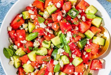 Watermelon Feta Salad served on a large white platter with crumbled feta, fresh mint, cucumber slices, and a drizzle of honey and lime juice, photographed overhead on a rustic wooden table in bright summer light