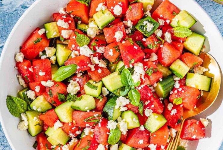 Watermelon Feta Salad served on a large white platter with crumbled feta, fresh mint, cucumber slices, and a drizzle of honey and lime juice, photographed overhead on a rustic wooden table in bright summer light