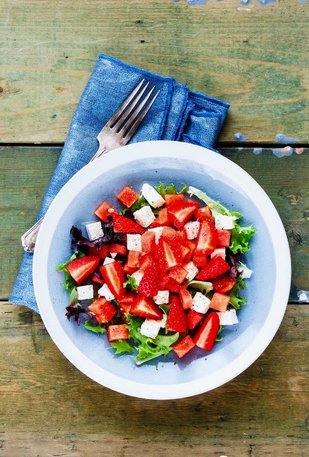 Overhead flat-lay of watermelon feta salad ingredients including a halved watermelon, block of feta in brine, fresh mint leaves, sliced cucumber, red onion, lime wedges, and a small jar of honey on a marble surface
