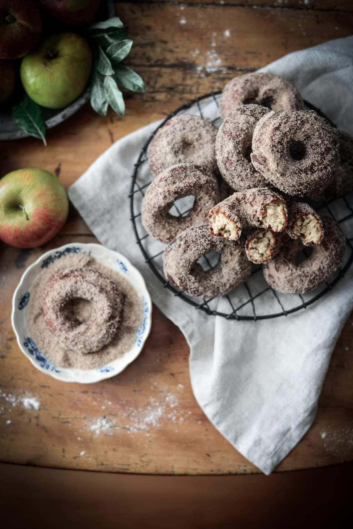 warm baked apple cider donuts coated in cinnamon sugar on a rustic wooden board with a glass of apple cider