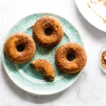 overhead flat lay of apple cider donut ingredients including reduced cider, spices, brown sugar, sour cream, and flour on a marble countertop