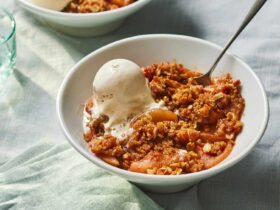 Golden apple crisp fresh from the oven in a white baking dish, topped with a thick buttery oat streusel, served warm with a scoop of vanilla ice cream melting over the top