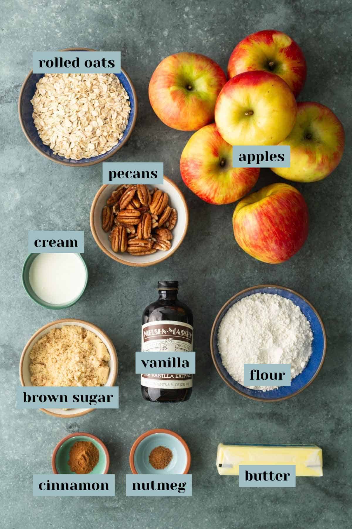 Overhead flat-lay of apple crisp ingredients including sliced Granny Smith and Honeycrisp apples, rolled oats, brown sugar, cinnamon sticks, cold butter cubes, and flour on a wooden surface