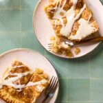 Overhead flat-lay of apple slab pie ingredients — sliced Granny Smith apples, brown sugar, cinnamon sticks, cold butter cubes, flour, and lemon on a marble surface