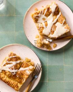 Overhead flat-lay of apple slab pie ingredients — sliced Granny Smith apples, brown sugar, cinnamon sticks, cold butter cubes, flour, and lemon on a marble surface
