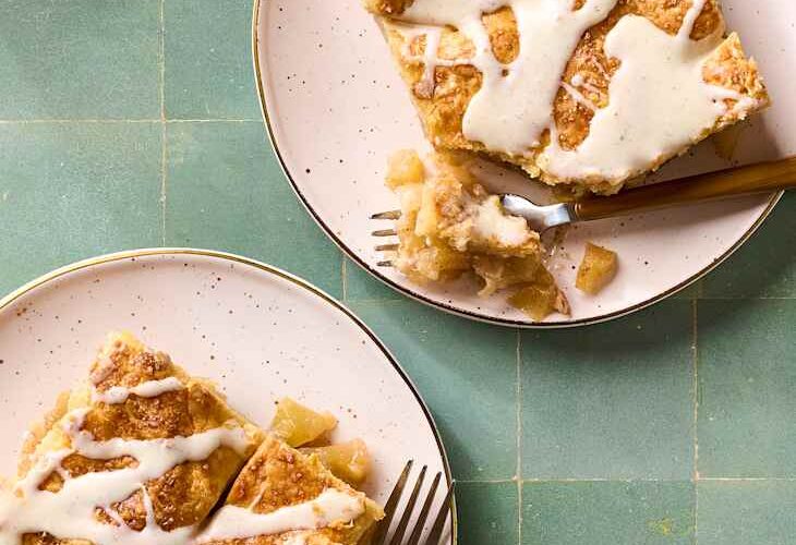 Overhead flat-lay of apple slab pie ingredients — sliced Granny Smith apples, brown sugar, cinnamon sticks, cold butter cubes, flour, and lemon on a marble surface