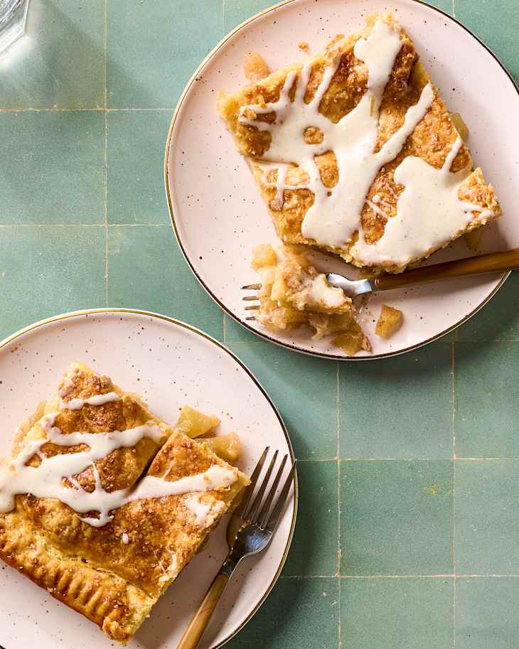 Overhead flat-lay of apple slab pie ingredients — sliced Granny Smith apples, brown sugar, cinnamon sticks, cold butter cubes, flour, and lemon on a marble surface