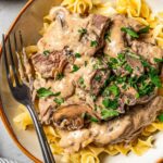 Beef stroganoff served over egg noodles in a wide bowl, topped with fresh parsley and cracked black pepper, rustic table setting