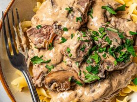 Beef stroganoff served over egg noodles in a wide bowl, topped with fresh parsley and cracked black pepper, rustic table setting