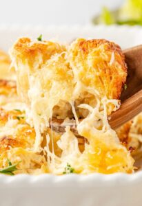Chicken alfredo bake in a golden bubbly casserole dish with melted mozzarella and parmesan crust, fresh parsley garnish, overhead shot on a rustic wooden table