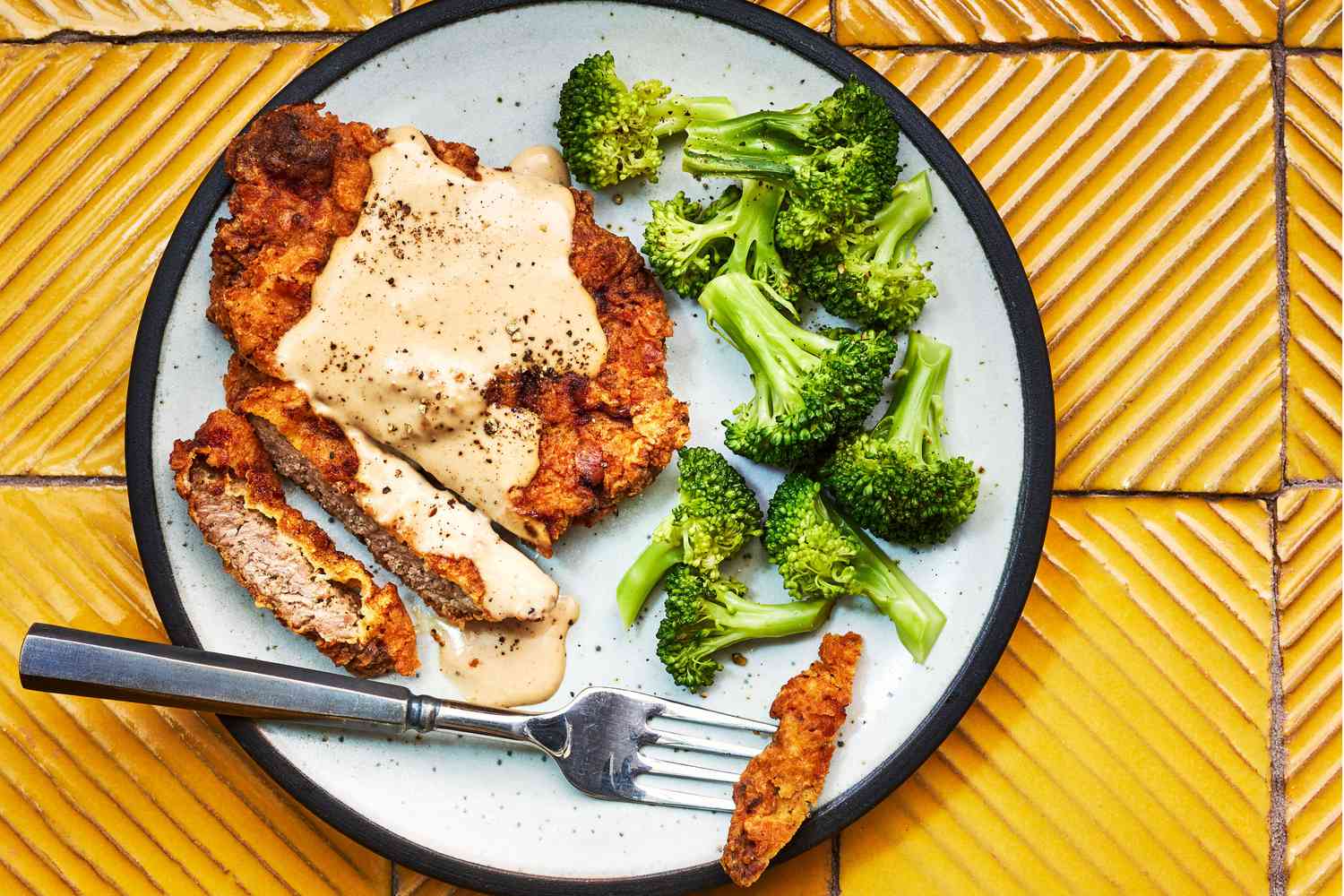 Close-up of chicken fried steak being cut open to reveal a tender interior with white gravy pooling on the plate