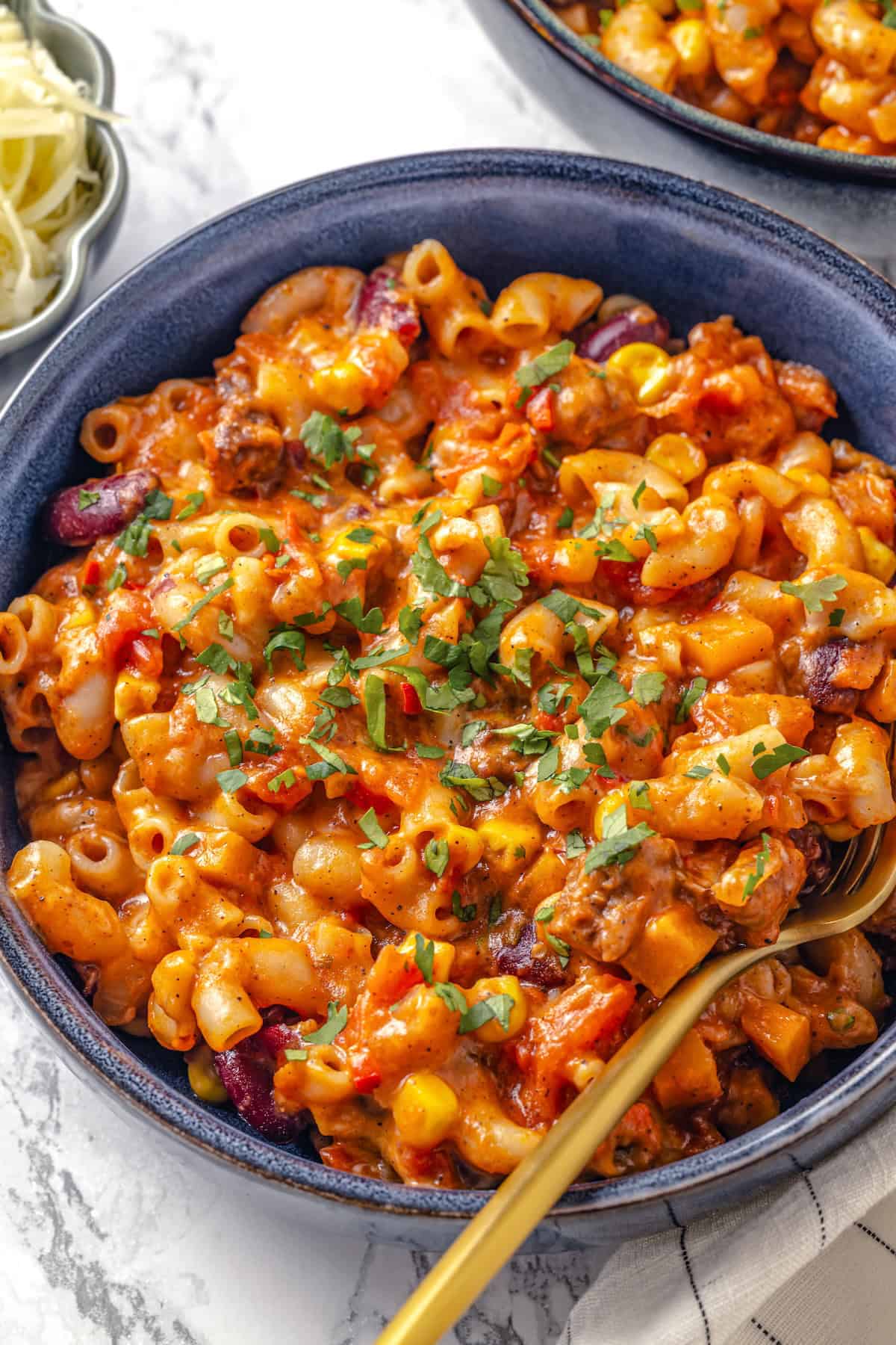 A rustic pot of chili mac with melted cheese and fresh toppings on a wooden table