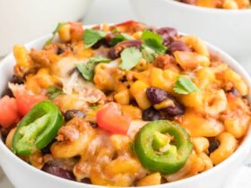 Close-up of a bowl of chili mac topped with melted cheddar, sour cream, and sliced jalapeños