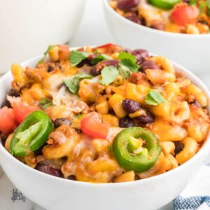 Close-up of a bowl of chili mac topped with melted cheddar, sour cream, and sliced jalapeños