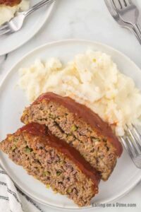 Close-up of a glazed meatloaf slice on a white plate with a fork, mashed potatoes in the background, warm and inviting lighting