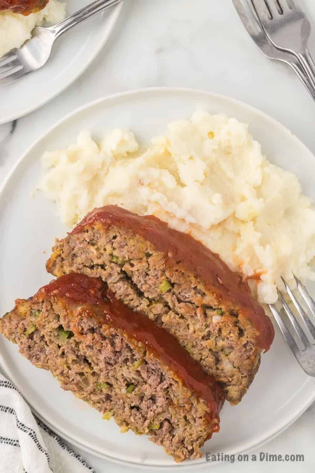 Close-up of a glazed meatloaf slice on a white plate with a fork, mashed potatoes in the background, warm and inviting lighting
