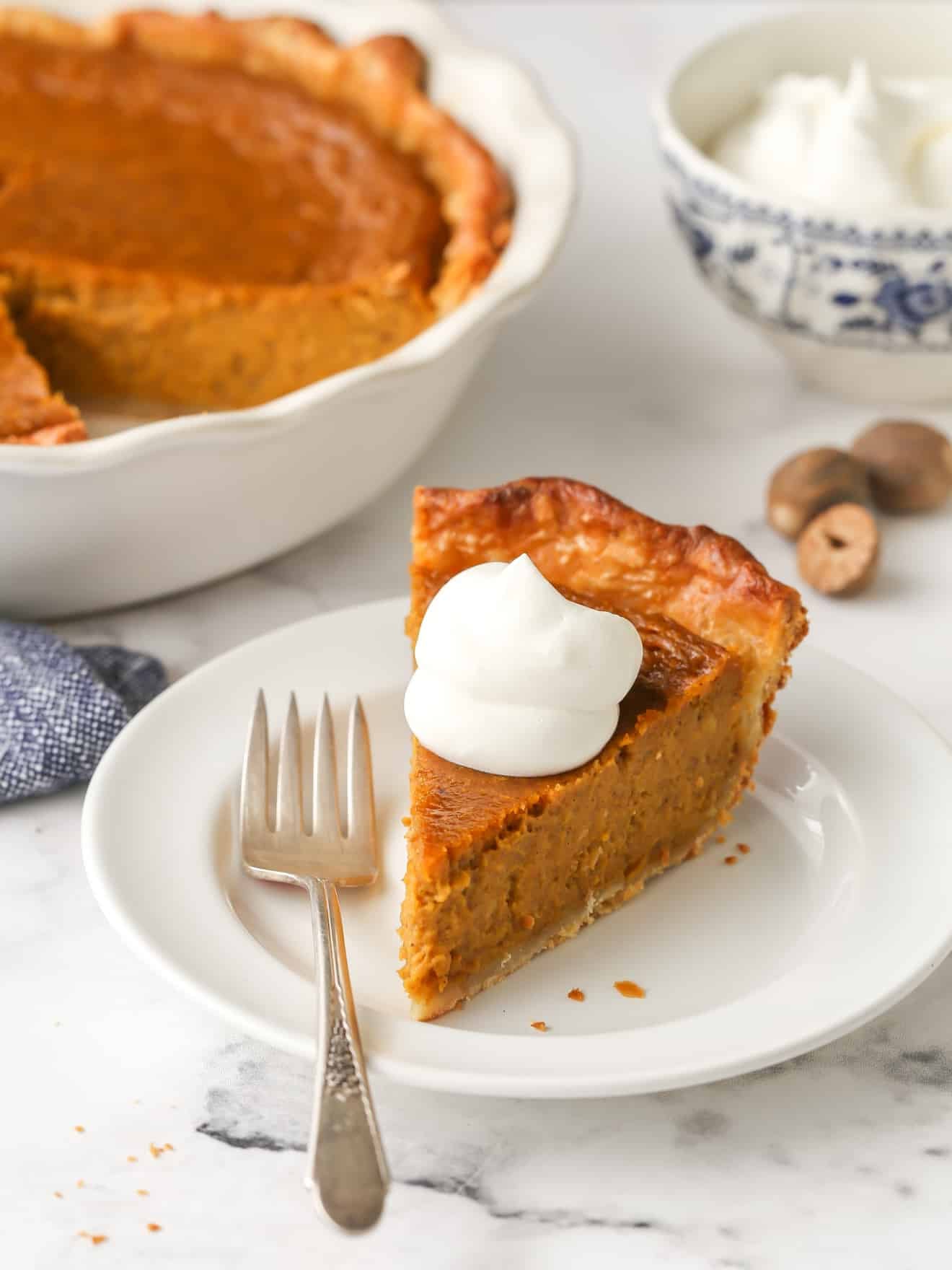 Classic pumpkin pie with a flaky all-butter crust, sliced and plated on a white plate with a dollop of whipped cream, golden autumn light