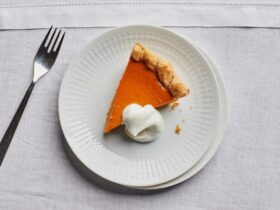 Close-up of a pumpkin pie slice on a fork, showing the smooth custard interior and flaky butter crust layers, whipped cream on top