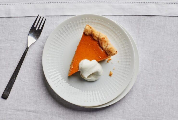 Close-up of a pumpkin pie slice on a fork, showing the smooth custard interior and flaky butter crust layers, whipped cream on top