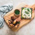 Crispy golden halloumi cheese fries served with a creamy yogurt dipping sauce and fresh herbs on a rustic wooden board